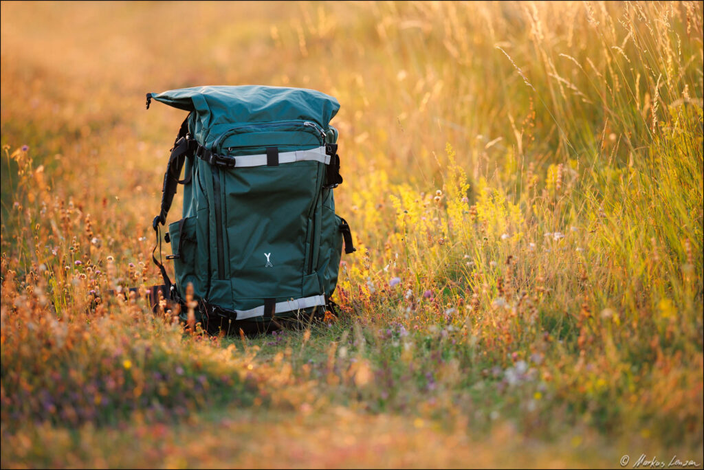 NYA-EVO Fjord 80L Abenteuer- und Kamera-Rucksack in Grün für Wildlife-Fotografen steht in der Sommerwiese.